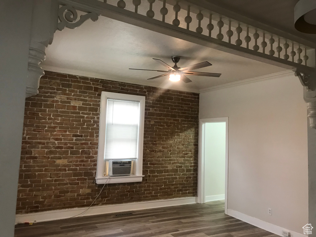Empty room featuring ornamental molding, dark hardwood / wood-style flooring, brick wall, and ceiling fan