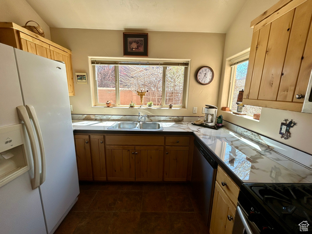Kitchen with dark tile flooring, dishwasher, white refrigerator with ice dispenser, and sink