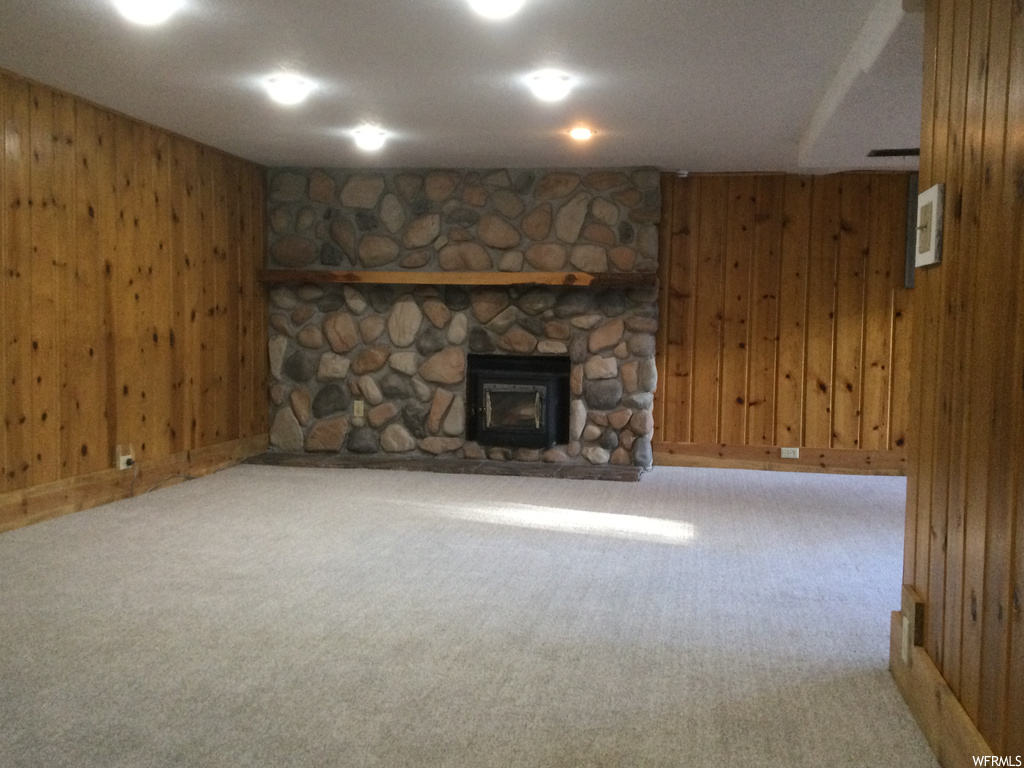 Unfurnished living room with wood walls, a stone fireplace, and light colored carpet