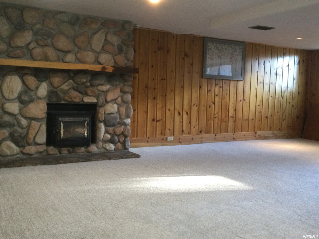 Unfurnished living room featuring wooden walls, a stone fireplace, and carpet floors