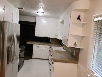 Kitchen featuring light wood-type flooring, stainless steel fridge with ice dispenser, white cabinets, sink, and a textured ceiling