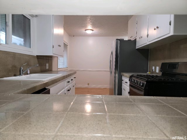 Kitchen featuring hardwood / wood-style floors, white cabinetry, black range with gas stovetop, backsplash, and sink