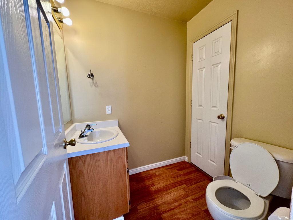 Bathroom featuring wood-type flooring, large vanity, toilet, and a textured ceiling