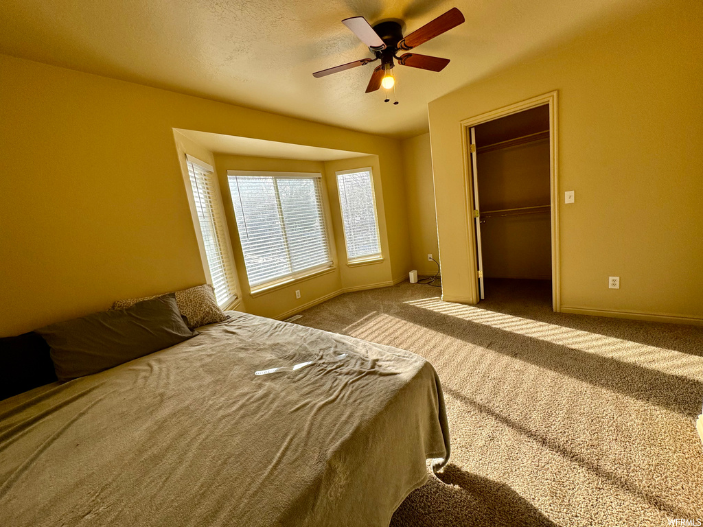 Unfurnished bedroom with light colored carpet, a closet, a spacious closet, and ceiling fan