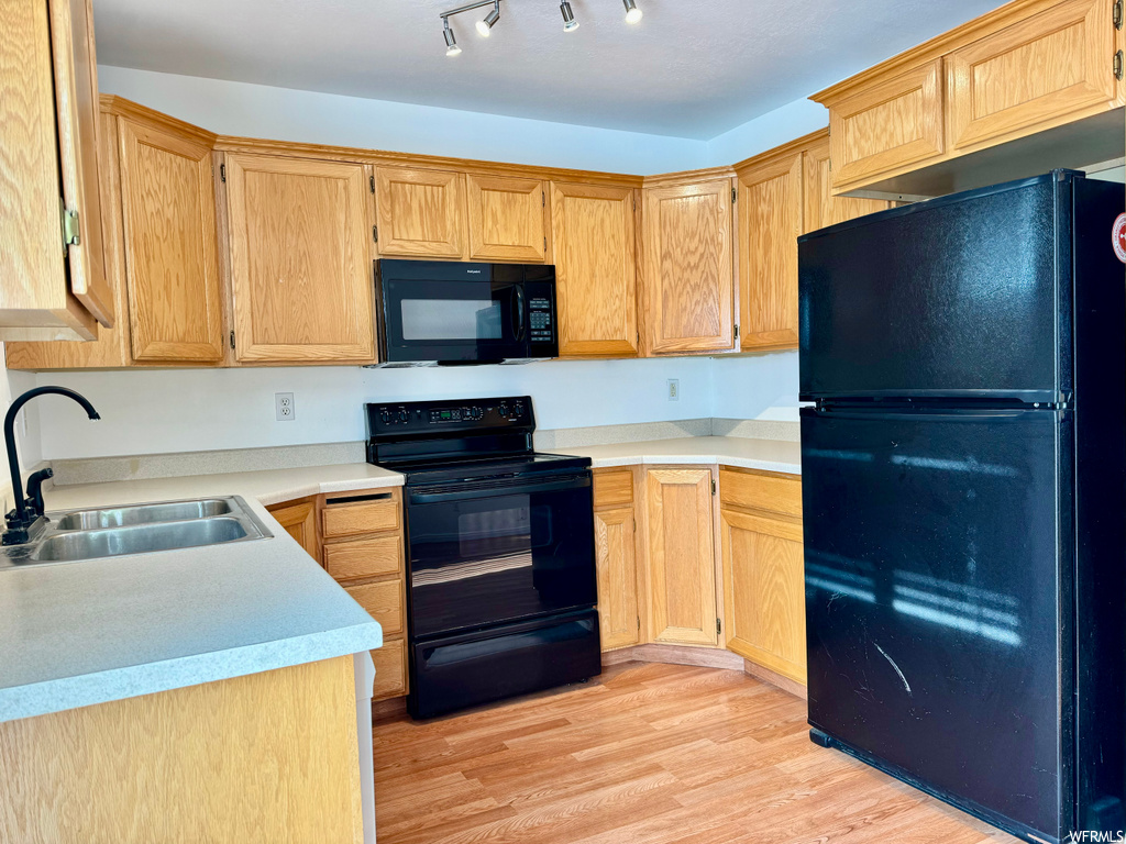 Kitchen featuring sink, track lighting, light hardwood / wood-style floors, and black appliances
