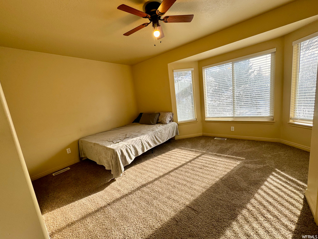 Unfurnished bedroom with multiple windows, dark colored carpet, and ceiling fan