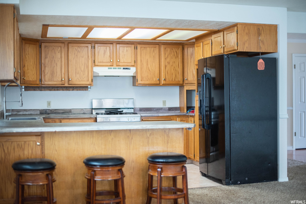 Kitchen featuring sink, white gas range, black fridge, and a kitchen bar