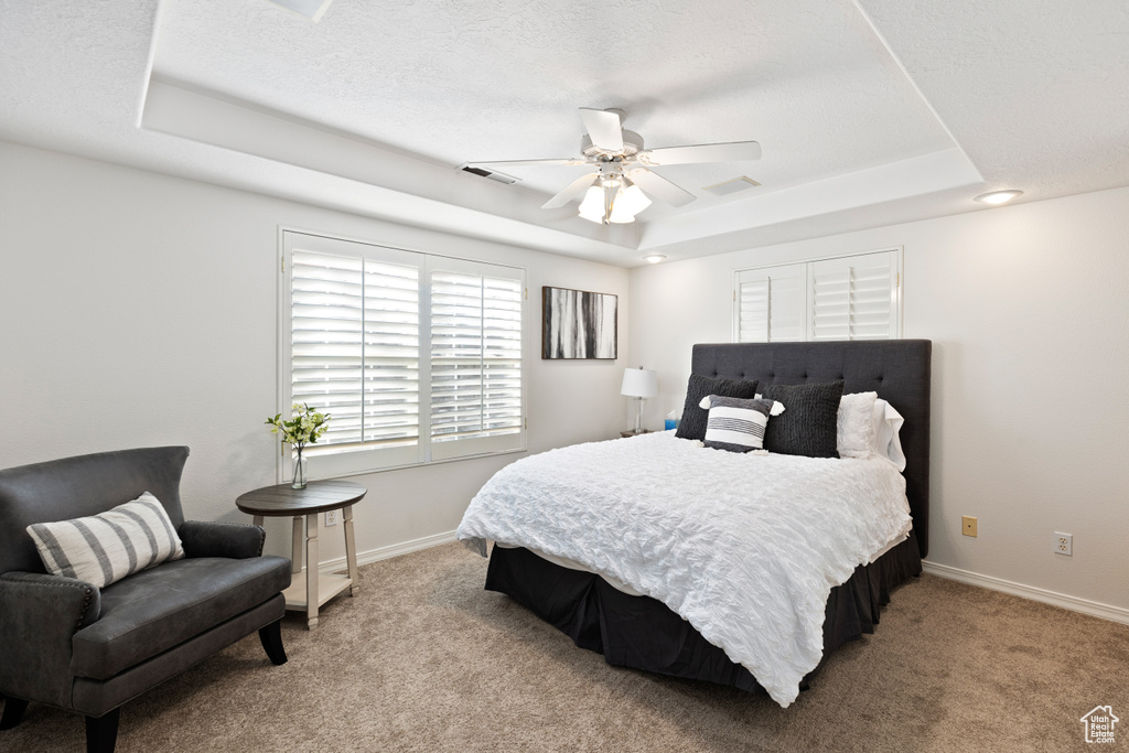 Bedroom with light carpet, a tray ceiling, and ceiling fan