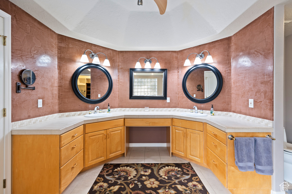 Bathroom with tile floors, double sink, vanity with extensive cabinet space, and ceiling fan