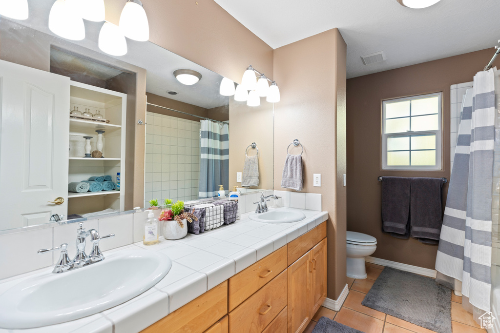Bathroom featuring toilet, double sink vanity, and tile flooring