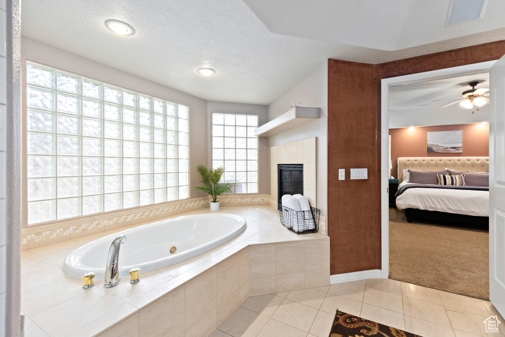 Bathroom featuring tiled bath, ceiling fan, tile flooring, a fireplace, and a textured ceiling