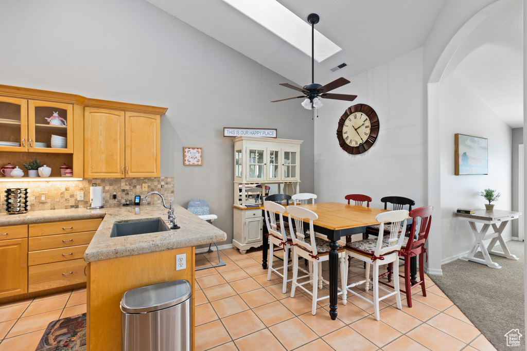 Kitchen featuring light tile flooring, a skylight, ceiling fan, sink, and high vaulted ceiling