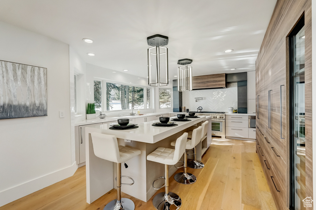 Kitchen featuring a breakfast bar area, a center island, light hardwood / wood-style flooring, backsplash, and white cabinetry