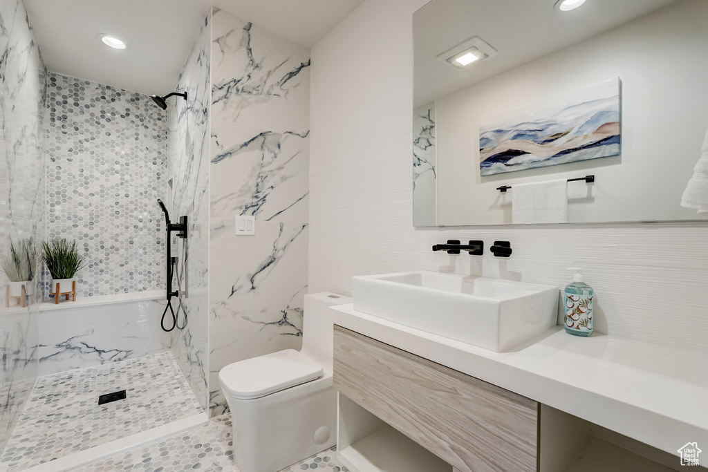 Bathroom featuring a tile shower, oversized vanity, tile walls, toilet, and backsplash