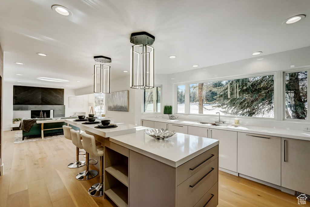 Kitchen with a kitchen bar, white cabinets, light hardwood / wood-style floors, a center island, and sink