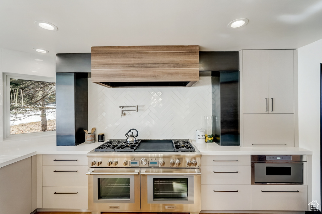 Kitchen featuring white cabinets, custom exhaust hood, appliances with stainless steel finishes, and backsplash