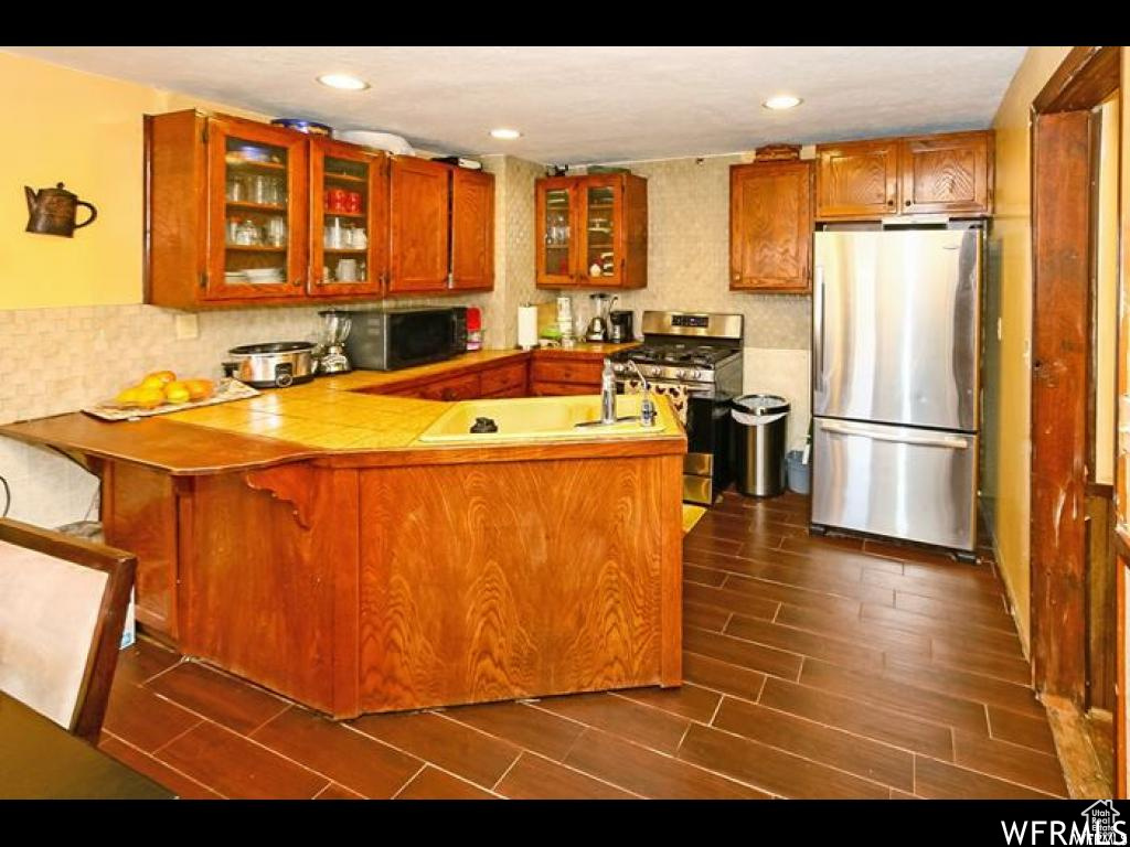 Kitchen featuring kitchen peninsula, a breakfast bar area, stainless steel appliances, tasteful backsplash, and dark wood-type flooring