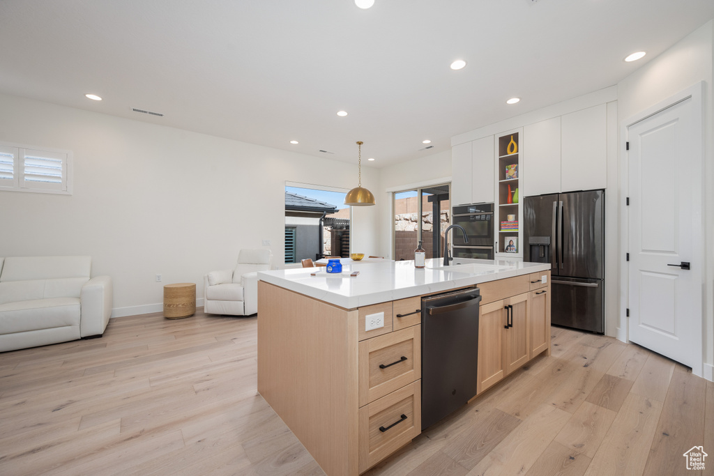 Kitchen featuring pendant lighting, stainless steel fridge with ice dispenser, light hardwood / wood-style floors, and an island with sink