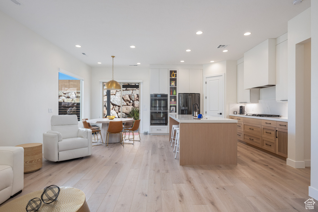 Kitchen featuring light hardwood / wood-style floors, a breakfast bar area, stainless steel refrigerator with ice dispenser, white cabinets, and an island with sink