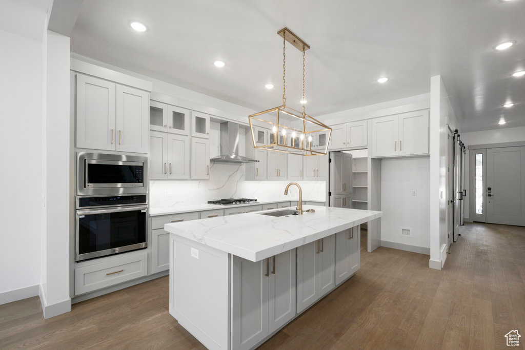 Kitchen featuring wall chimney exhaust hood, appliances with stainless steel finishes, sink, a center island with sink, and hardwood / wood-style floors