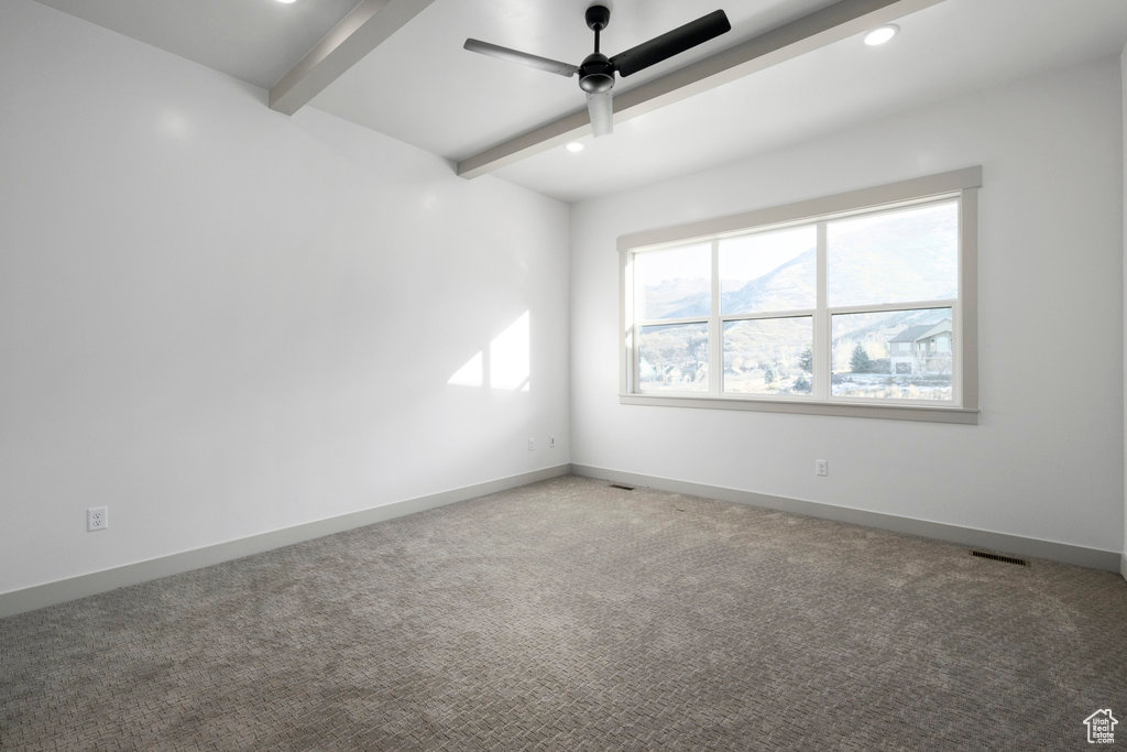Carpeted empty room featuring beam ceiling and ceiling fan