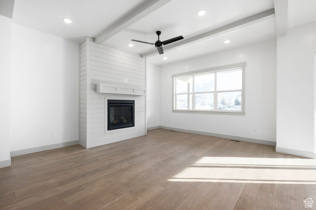 Unfurnished living room with beam ceiling, light hardwood / wood-style flooring, a fireplace, and ceiling fan