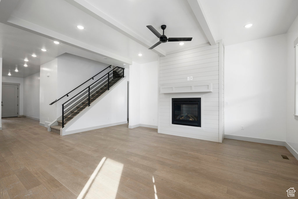 Unfurnished living room with light wood-type flooring, beamed ceiling, a fireplace, and ceiling fan