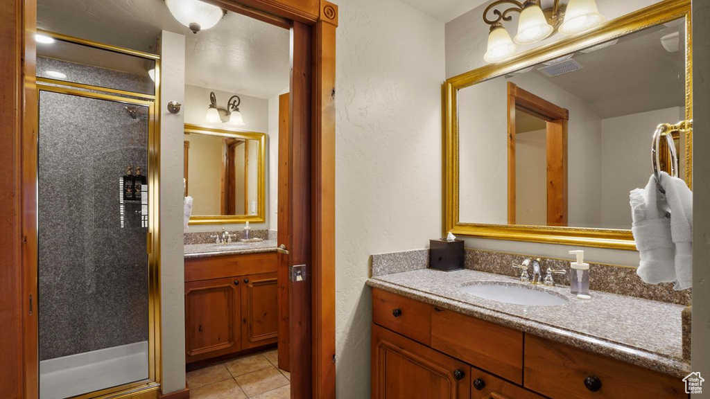 Bathroom with a shower with shower door, tile floors, dual sinks, and large vanity
