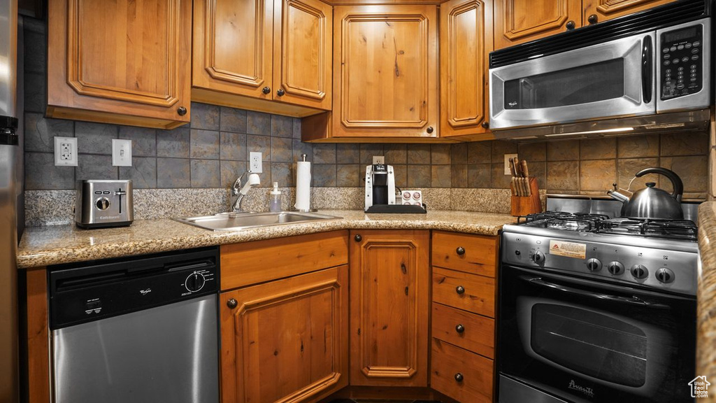 Kitchen featuring sink, light stone counters, appliances with stainless steel finishes, and backsplash