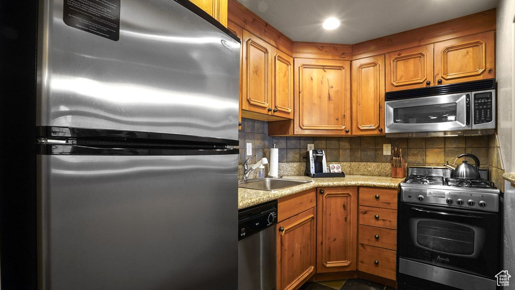 Kitchen featuring sink, stainless steel appliances, tasteful backsplash, and light stone countertops