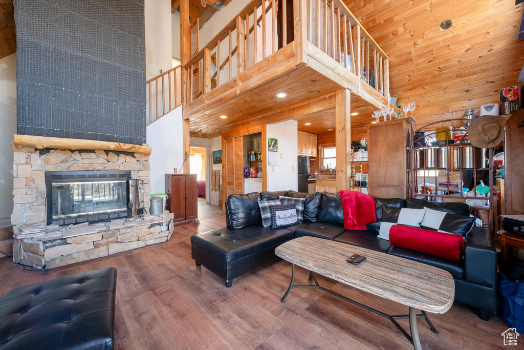 Living room with a stone fireplace, a towering ceiling, wood walls, and hardwood / wood-style floors