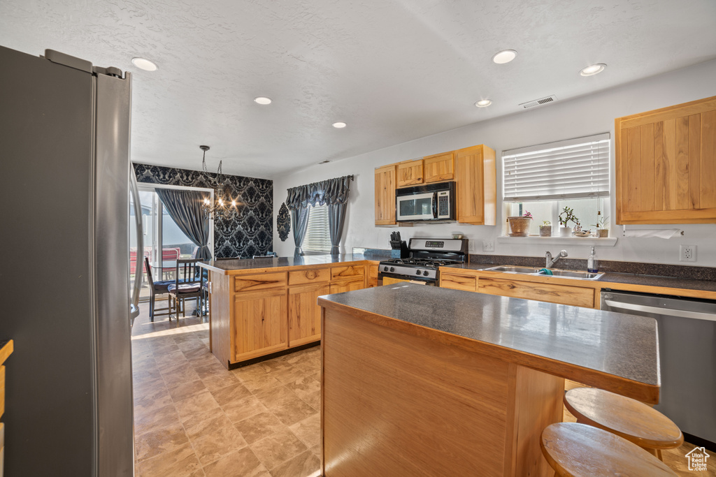 Kitchen featuring a kitchen bar, hanging light fixtures, stainless steel appliances, a notable chandelier, and sink