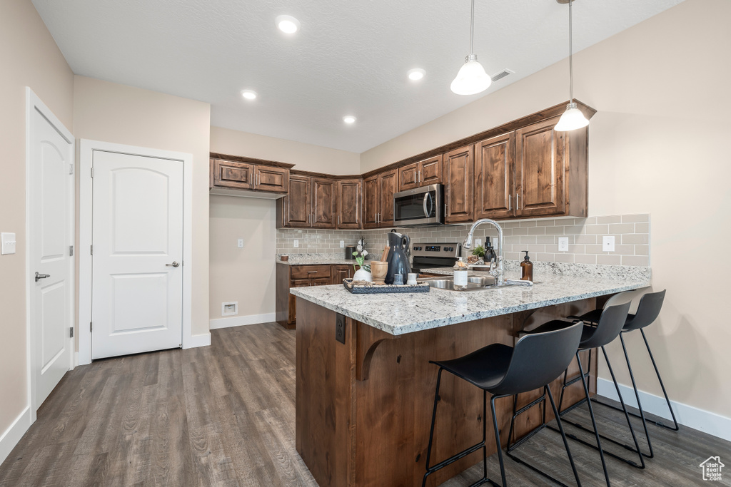 Kitchen featuring hanging light fixtures, appliances with stainless steel finishes, light stone countertops, dark hardwood / wood-style floors, and backsplash