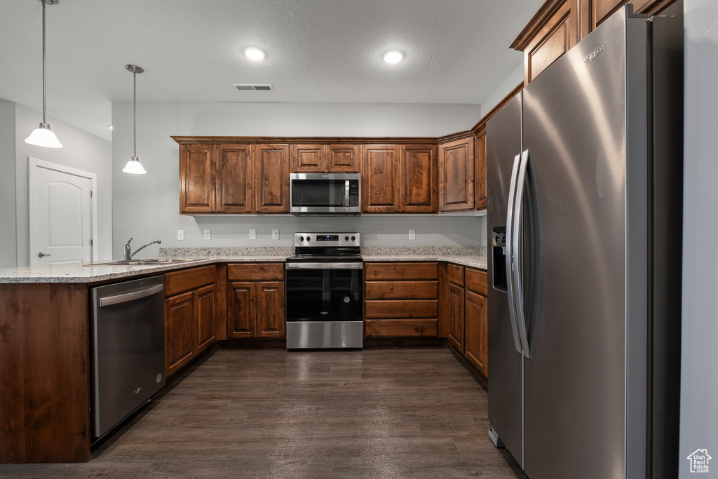 Kitchen featuring sink, appliances with stainless steel finishes, light stone countertops, dark hardwood / wood-style floors, and decorative light fixtures