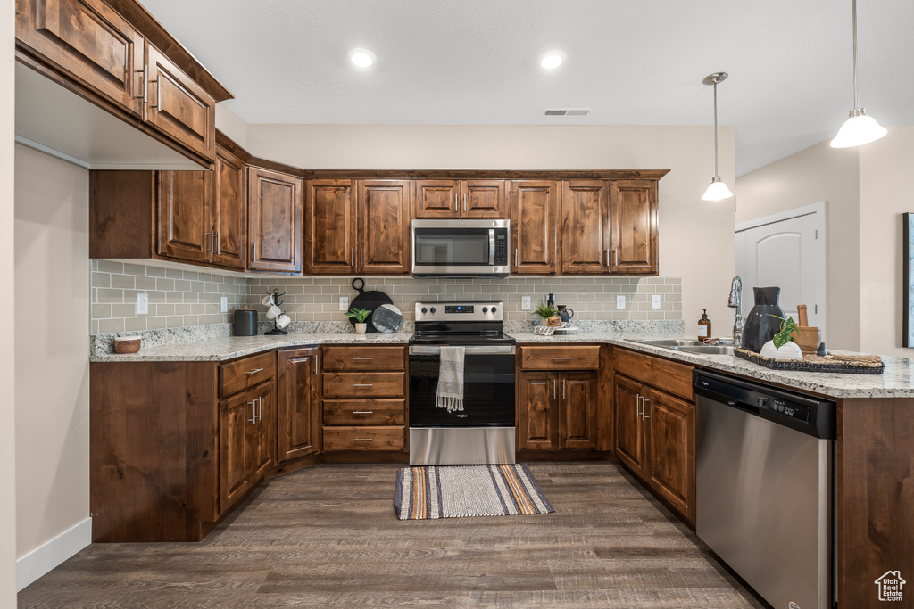 Kitchen featuring hanging light fixtures, sink, stainless steel appliances, tasteful backsplash, and dark hardwood / wood-style flooring