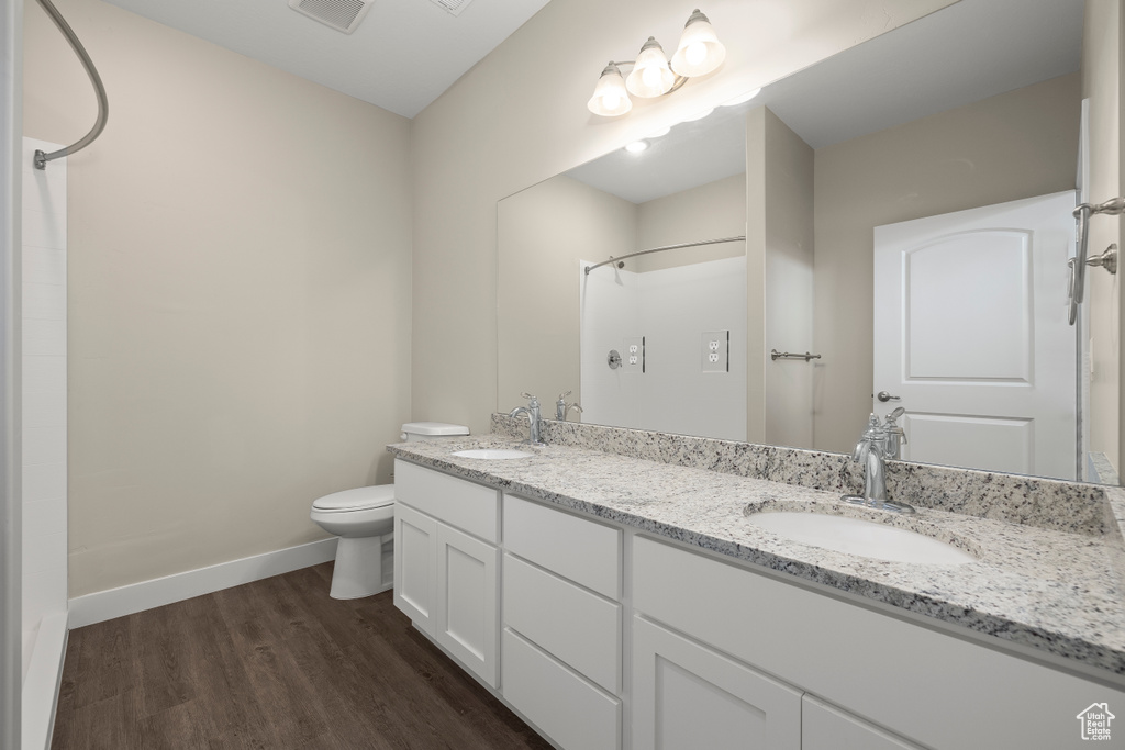 Bathroom with hardwood / wood-style floors, toilet, vanity with extensive cabinet space, and dual sinks