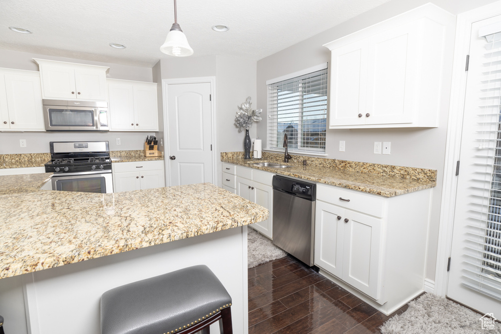 Kitchen featuring white cabinetry, appliances with stainless steel finishes, and decorative light fixtures