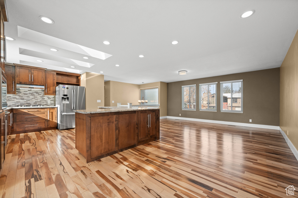 Kitchen featuring light stone countertops, light hardwood / wood-style floors, a skylight, stainless steel refrigerator with ice dispenser, and tasteful backsplash