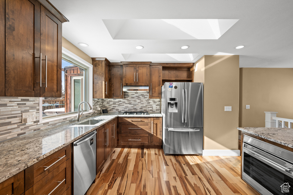 Kitchen with light hardwood / wood-style floors, appliances with stainless steel finishes, light stone countertops, and backsplash