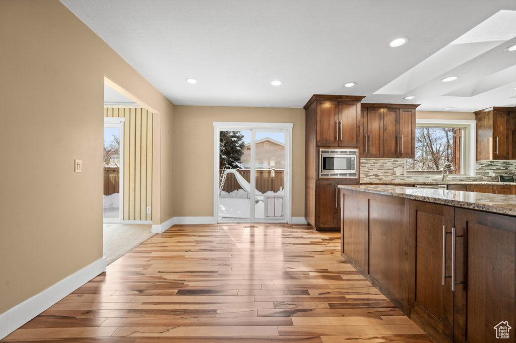 Kitchen with light hardwood / wood-style floors, stainless steel microwave, light stone countertops, and backsplash