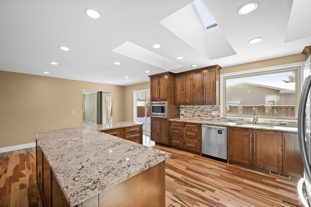 Kitchen featuring tasteful backsplash, light stone counters, a skylight, appliances with stainless steel finishes, and light hardwood / wood-style flooring
