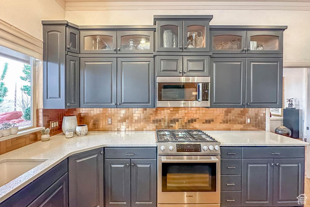 Kitchen featuring gray cabinetry, backsplash, appliances with stainless steel finishes, and light stone counters