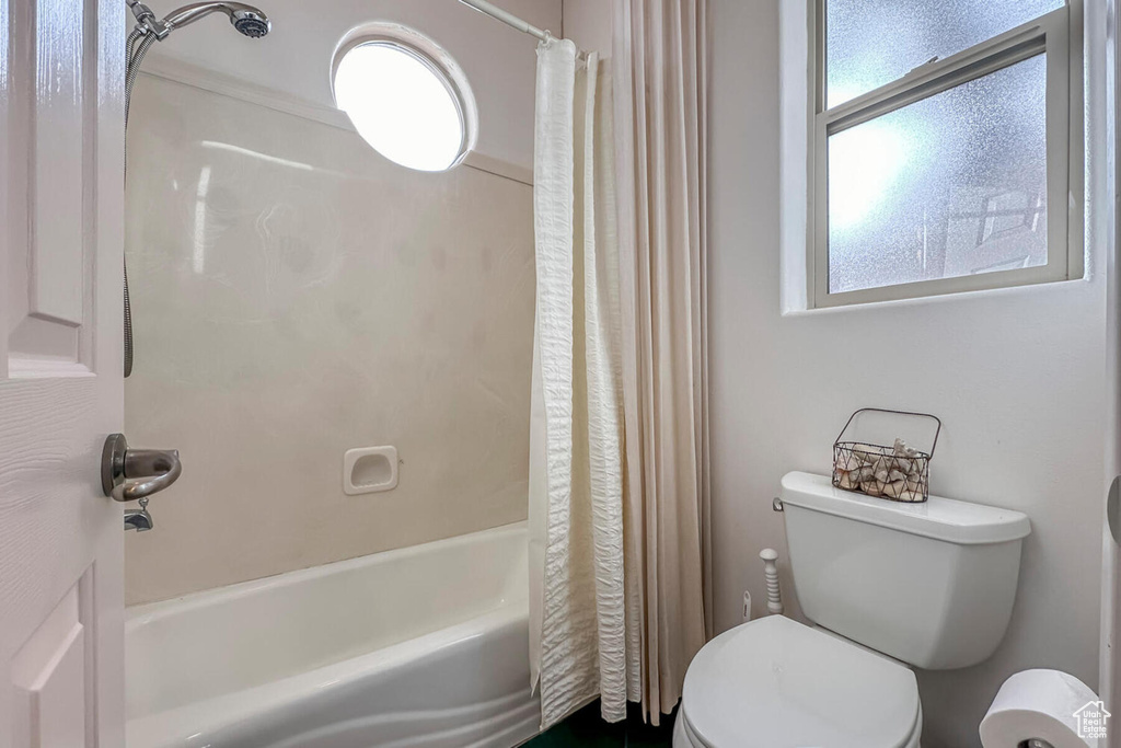 Bathroom with toilet, shower / bath combo with shower curtain, and a healthy amount of sunlight