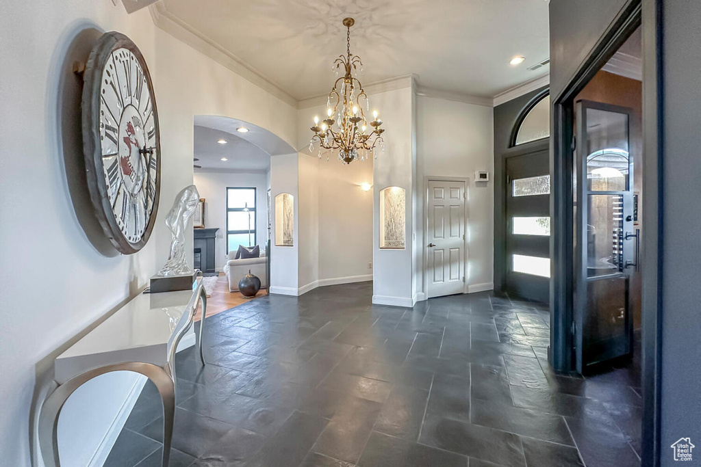 Entrance foyer with a notable chandelier, ornamental molding, and dark tile flooring