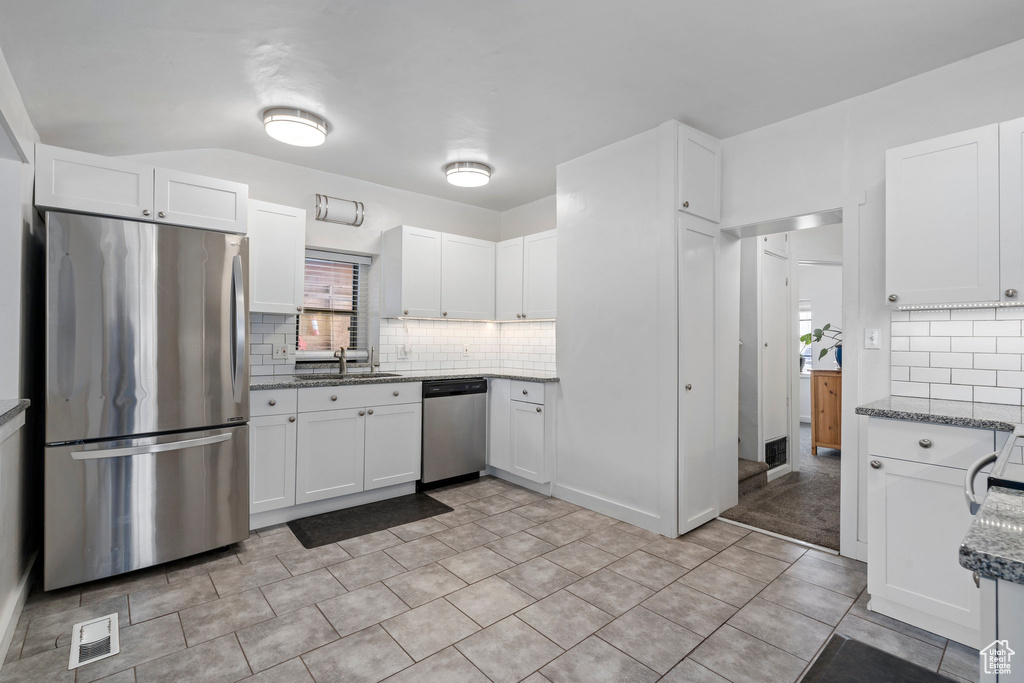 Kitchen featuring light tile flooring, white cabinets, dark stone counters, and stainless steel appliances