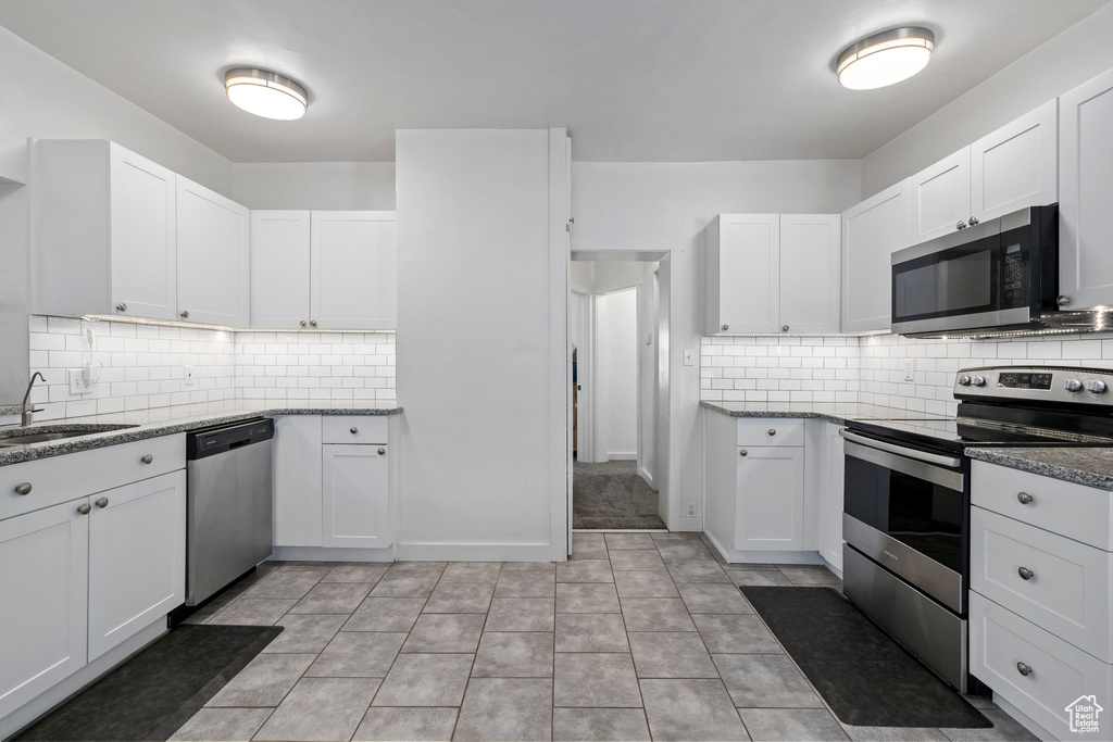 Kitchen featuring tasteful backsplash, stainless steel appliances, white cabinets, and light tile floors