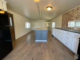 Kitchen featuring black refrigerator, white cabinetry, vaulted ceiling, and light hardwood / wood-style floors