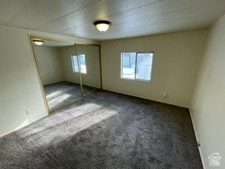Unfurnished bedroom with multiple windows, dark carpet, and a closet