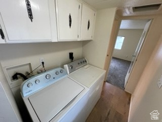 Clothes washing area with dark hardwood / wood-style flooring, cabinets, washing machine and dryer, and hookup for a washing machine