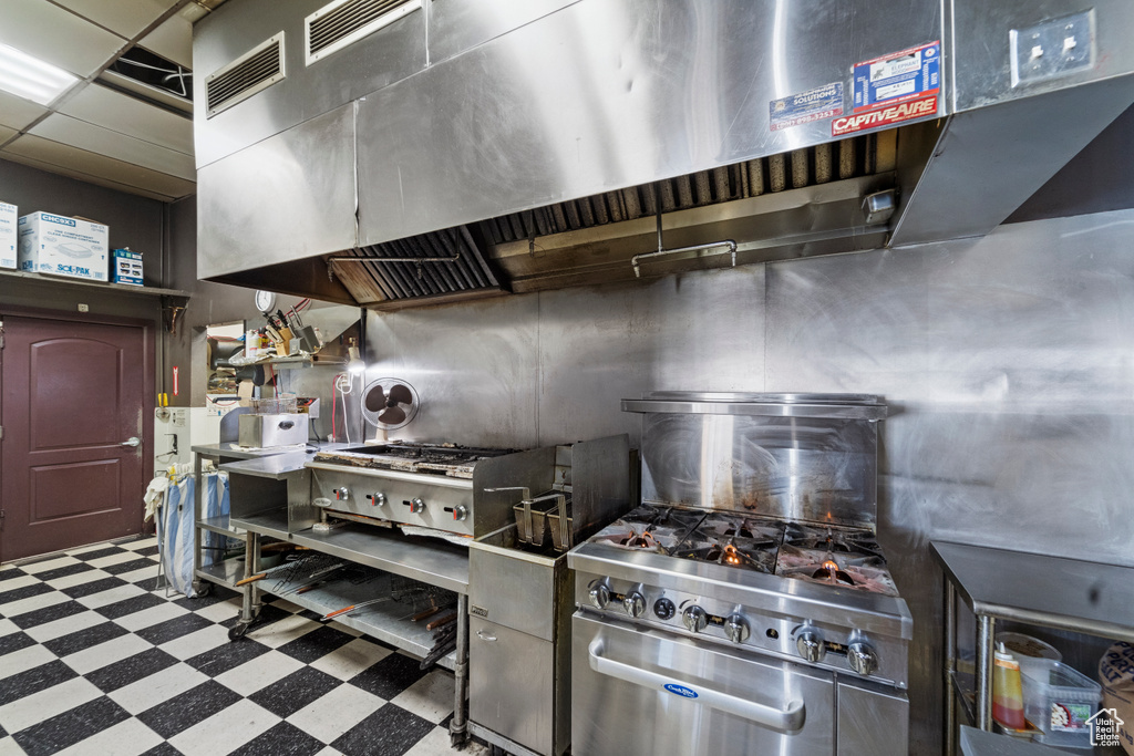 Kitchen featuring wall chimney exhaust hood, stainless steel counters, and light tile floors